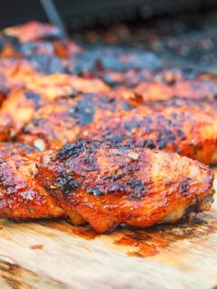 Sriracha glazed grilled chicken wings on a wooden chopping board with a bbq in the background