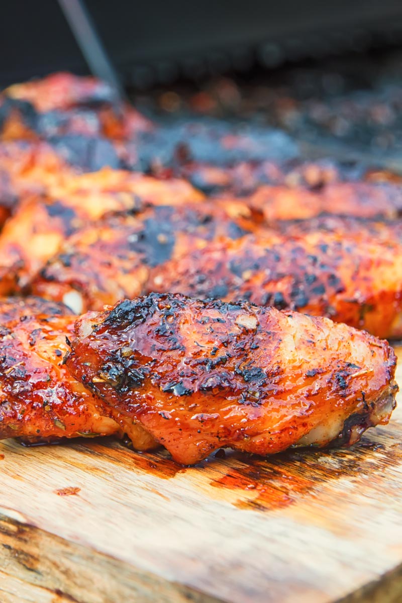 Sriracha glazed grilled chicken wings on a wooden chopping board with a bbq in the background