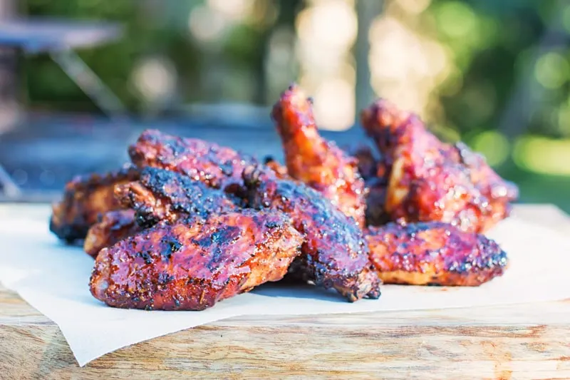 Landscape image of a pile of sriracha sauce glazed chicken wings on a wooden chopping board