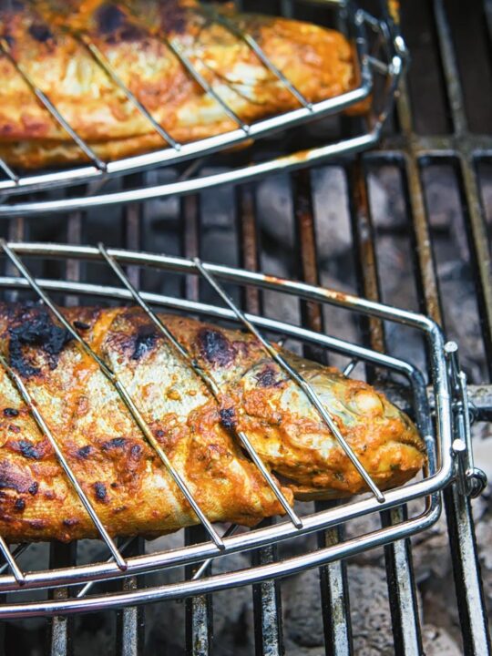 A whole BBQ tandoori fish cooking over hot coals in a fish cage