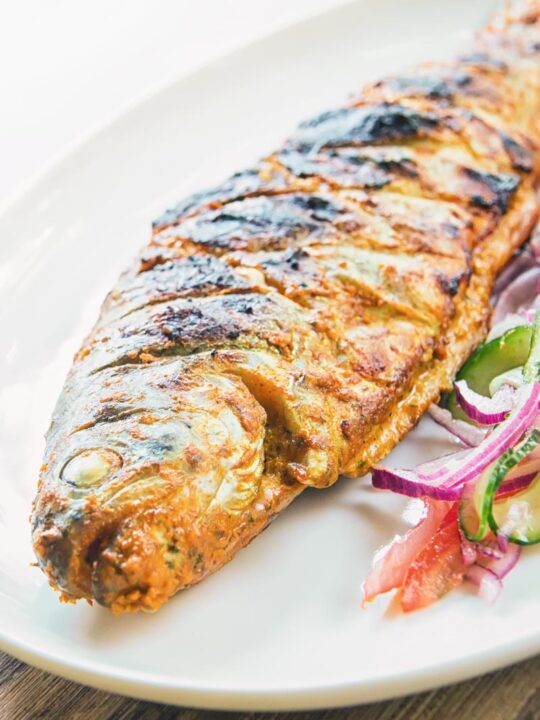 A whole BBQ tandoori fish with a kachumber salad on an oval plate