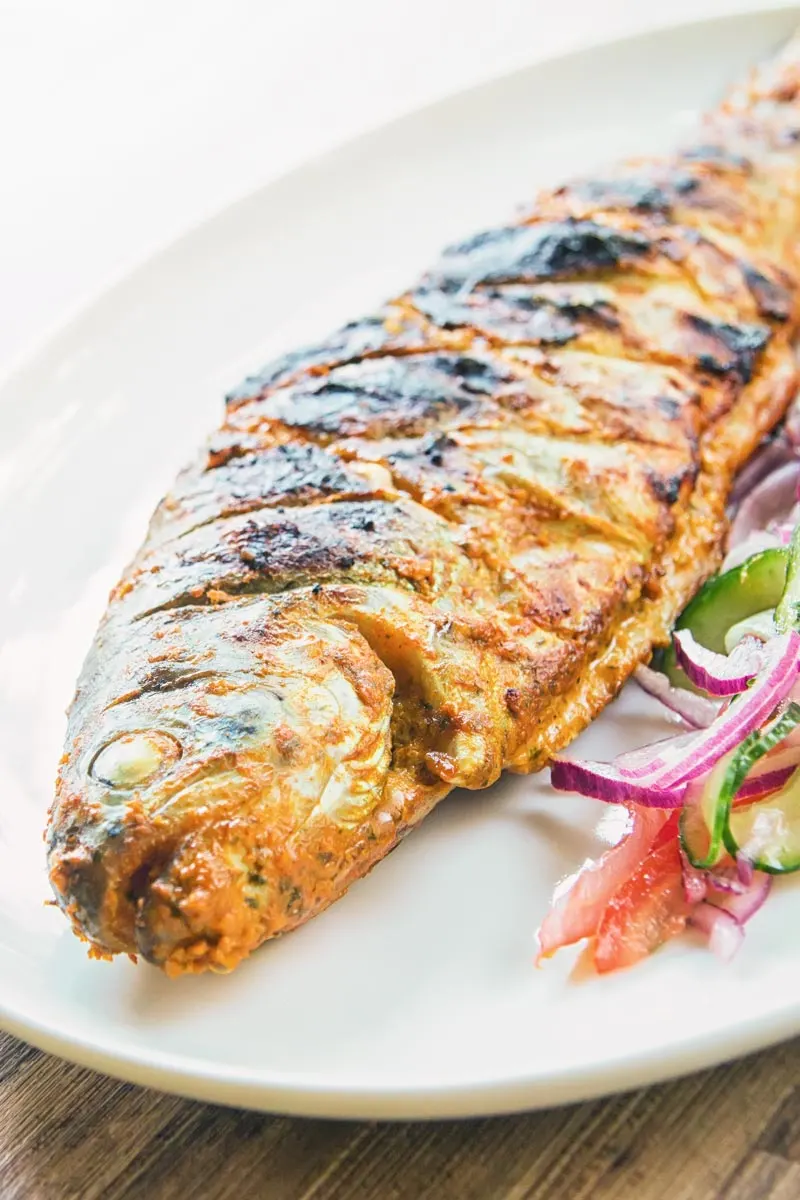 A whole BBQ tandoori fish with a kachumber salad on an oval plate