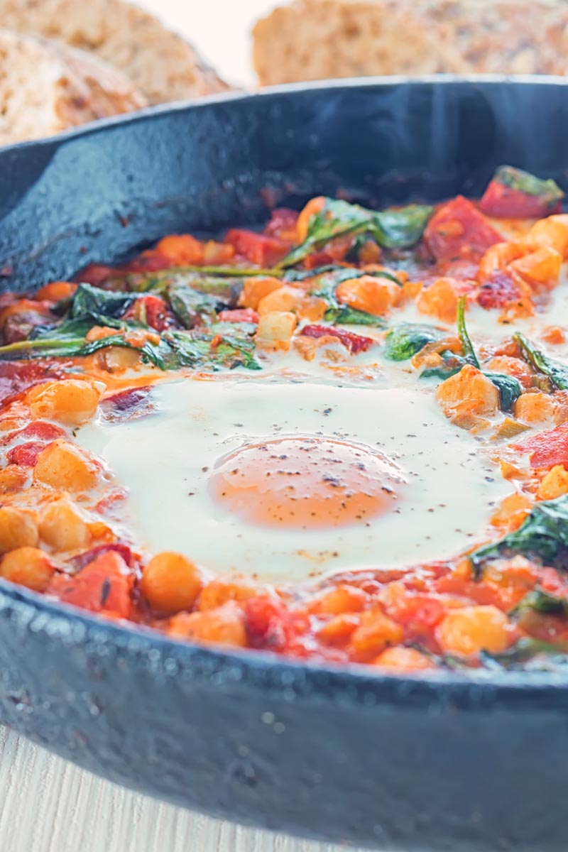 Close up portrait image of eggs in a tomato sauce and baked chickpeas served and cooked in a cast iron skillet
