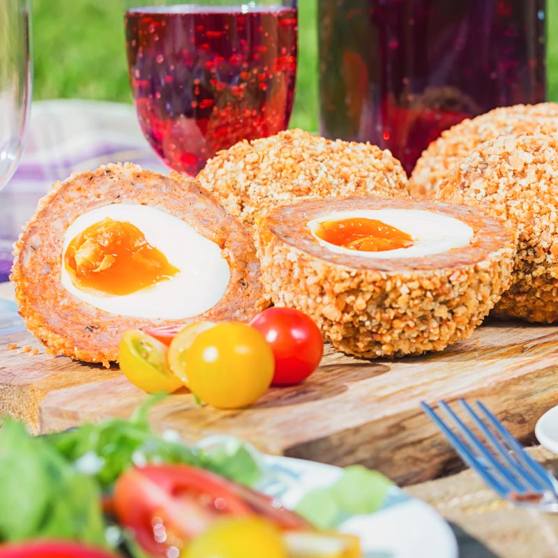 Close up square image of baked scotch eggs with one cut open in a picnic setting
