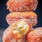 Portrait Image of cinnamon sugar coated donuts with a bite out of one cooked from a basic donut recipe
