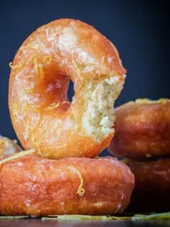 Portrait Image of lemon glazed ring donuts with a bite out of one cooked from a basic donut recipe