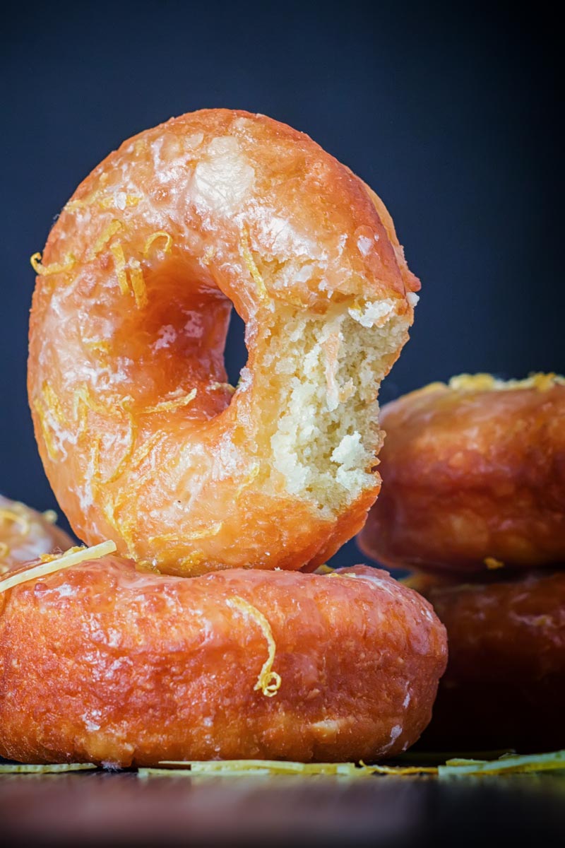 Portrait Image of lemon glazed ring donuts with a bite out of one cooked from a basic donut recipe