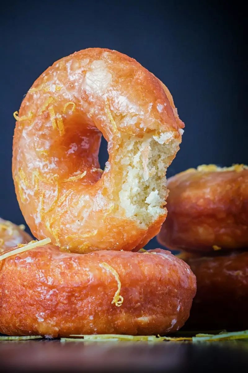 Portrait Image of lemon glazed ring donuts with a bite out of one cooked from a basic donut recipe