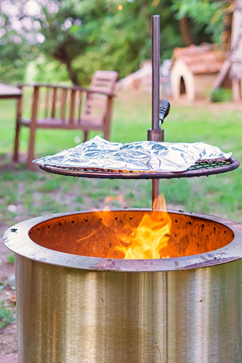 Portrait image of foil packets baking over a fire pit on a summers day