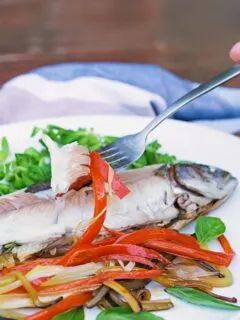 Portrait image of a fork showing the moist cooked flesh of a whole fish baked in foil with vegetable ribbons and salad