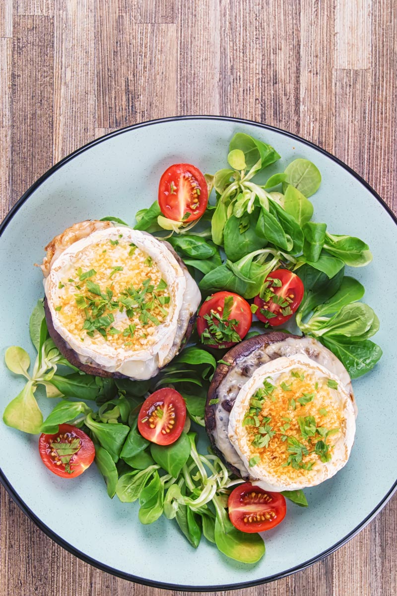 Over head portrait image of stuffed portobello mushrooms with goats cheese and a breadcrumb topping served with a green salad and tomatoes