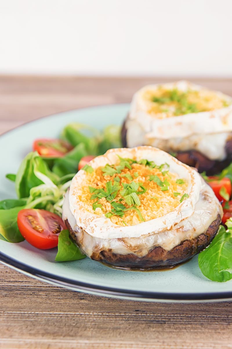 Portrait image of stuffed portobello mushrooms with goats cheese and a breadcrumb topping served with a green salad and tomatoes