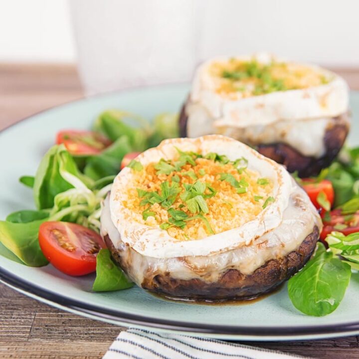Square image of stuffed portobello mushrooms with goats cheese and a breadcrumb topping served with a green salad and tomatoes