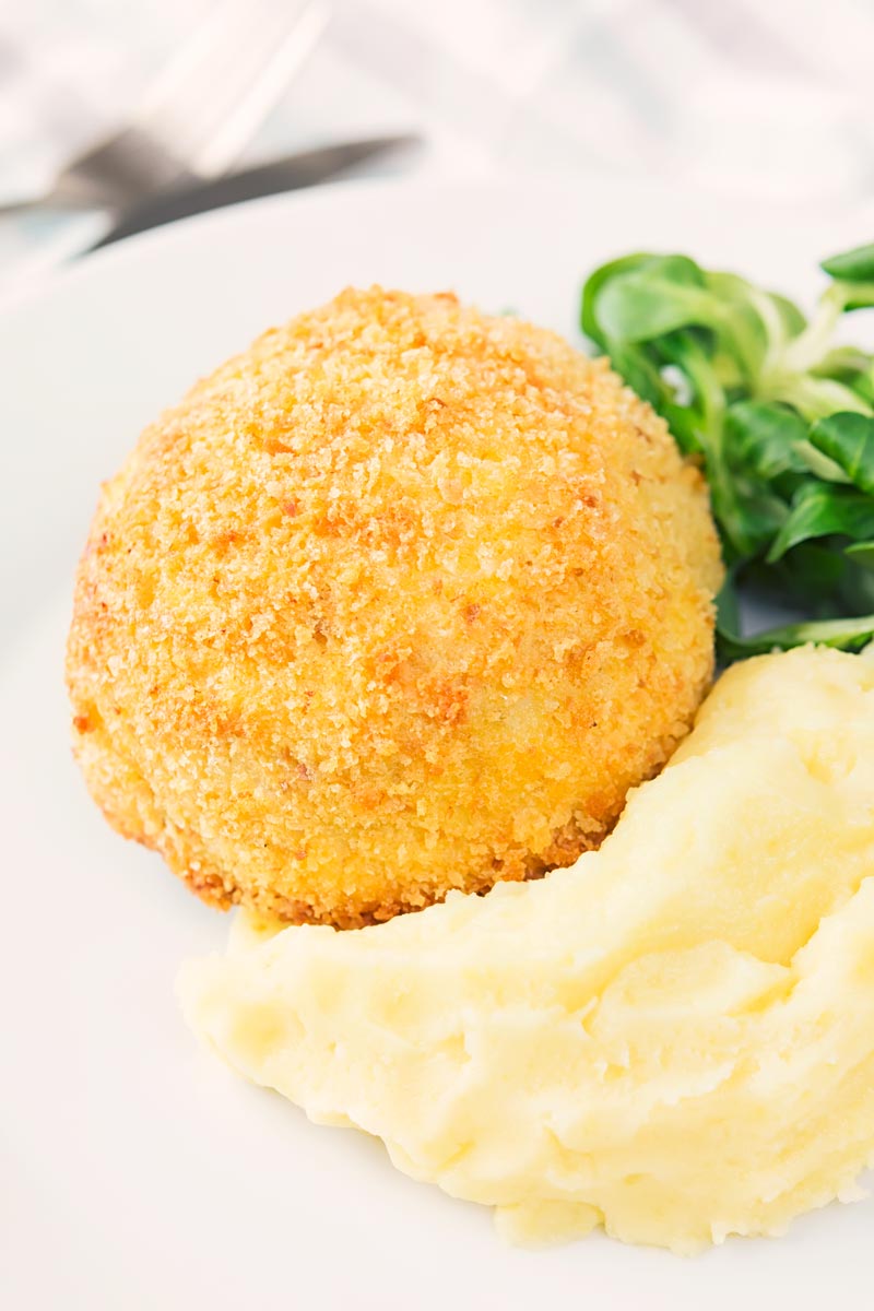 Portrait image of a crispy garlic chicken Kiev on a white plate, served with a side salad and mashed potato
