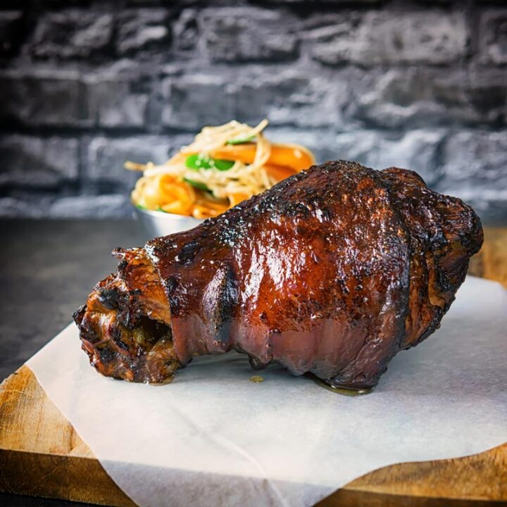 Square image of a braised and then glazed Chinese ham hock on a chopping board