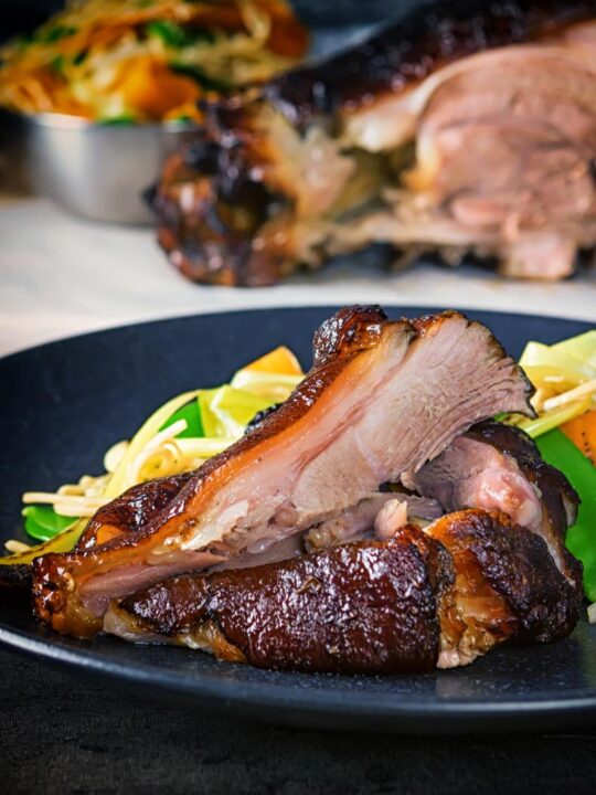 Tall image of meat taken from a Chinese braised ham hock on a black plate