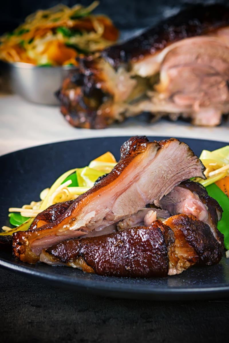 Tall image of meat taken from a Chinese braised ham hock on a black plate