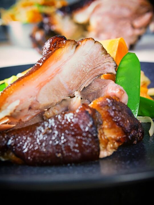 Tall close up image of meat taken from a Chinese braised ham hock on a black plate