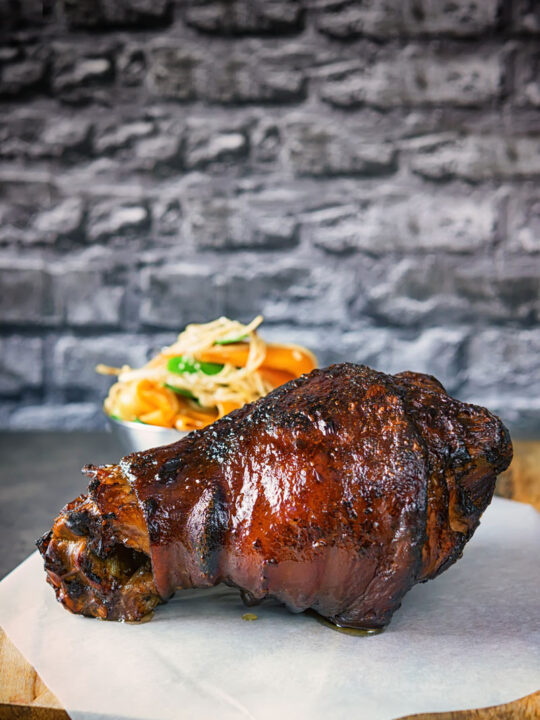 Tall image of a braised and then glazed Chinese ham hock on a chopping board