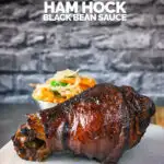 Tall image of a braised and then glazed Chinese ham hock on a chopping board with text