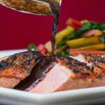 Vertical image of duck with plum sauce against a red background