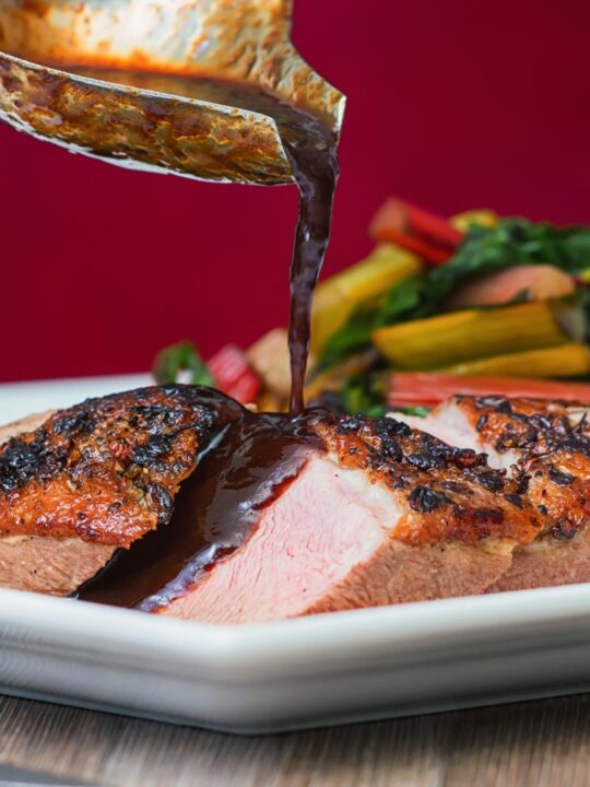 Portrait image of a sliced duck breast being covered in plum sauce from a ladle