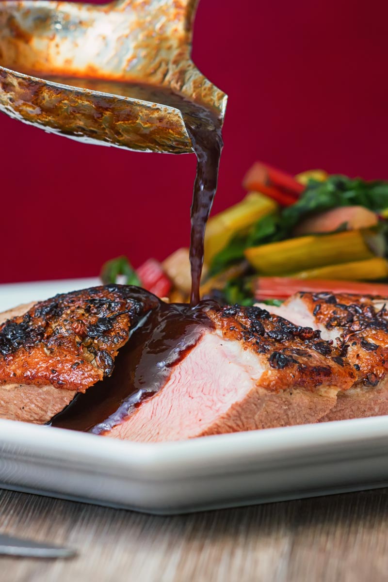 Portrait image of a sliced duck breast being covered in plum sauce from a ladle