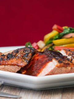 Vertical image of duck with plum sauce against a red background