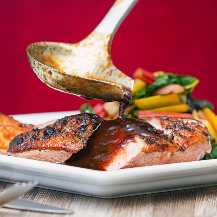 Square image of duck with plum sauce with the plum sauce being poured from a ladle