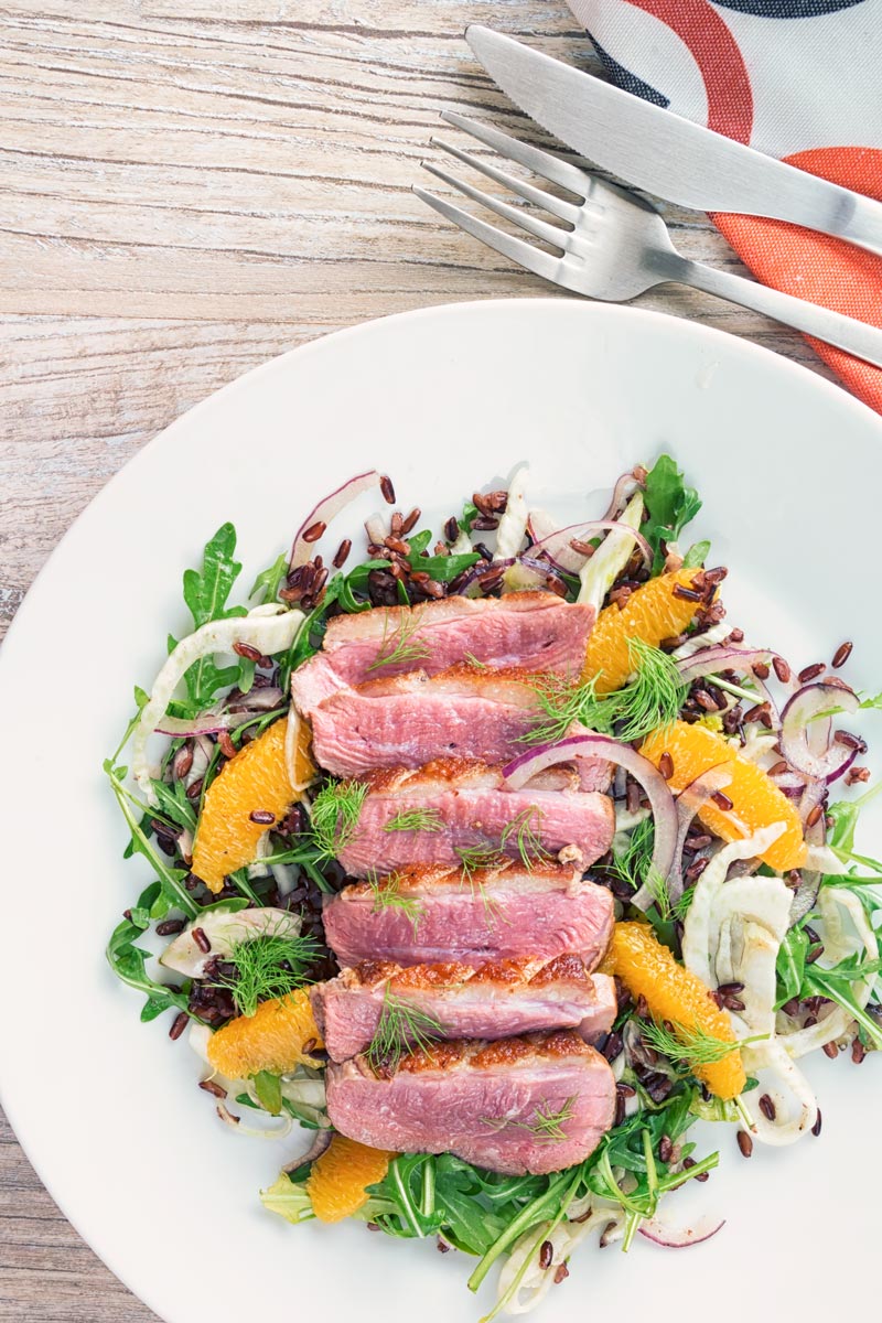 Portrait overhead image of a fennel and orange salad served with a sliced rosy pink duck breast served on a white plate