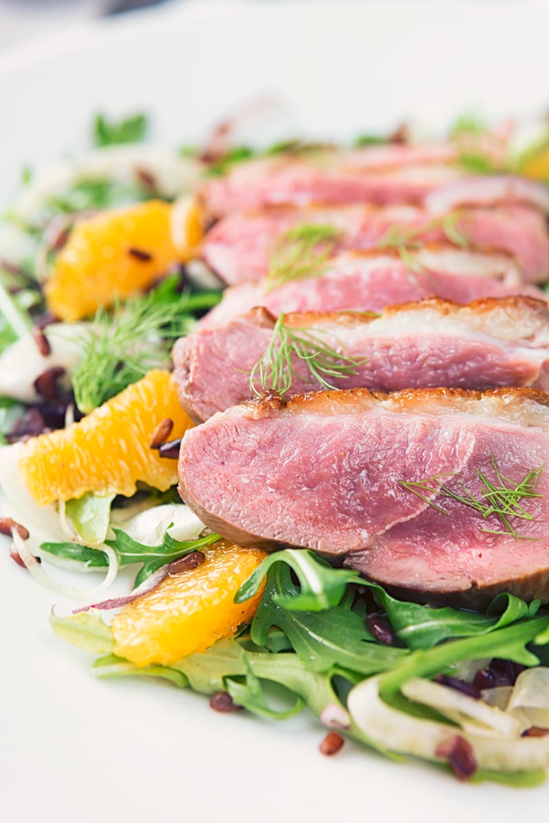 Portrait close up image of a fennel and orange salad served with a sliced rosy pink duck breast served on a white plate