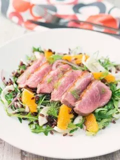 Portrait image of a fennel and orange salad served with a sliced rosy pink duck breast served on a white plate