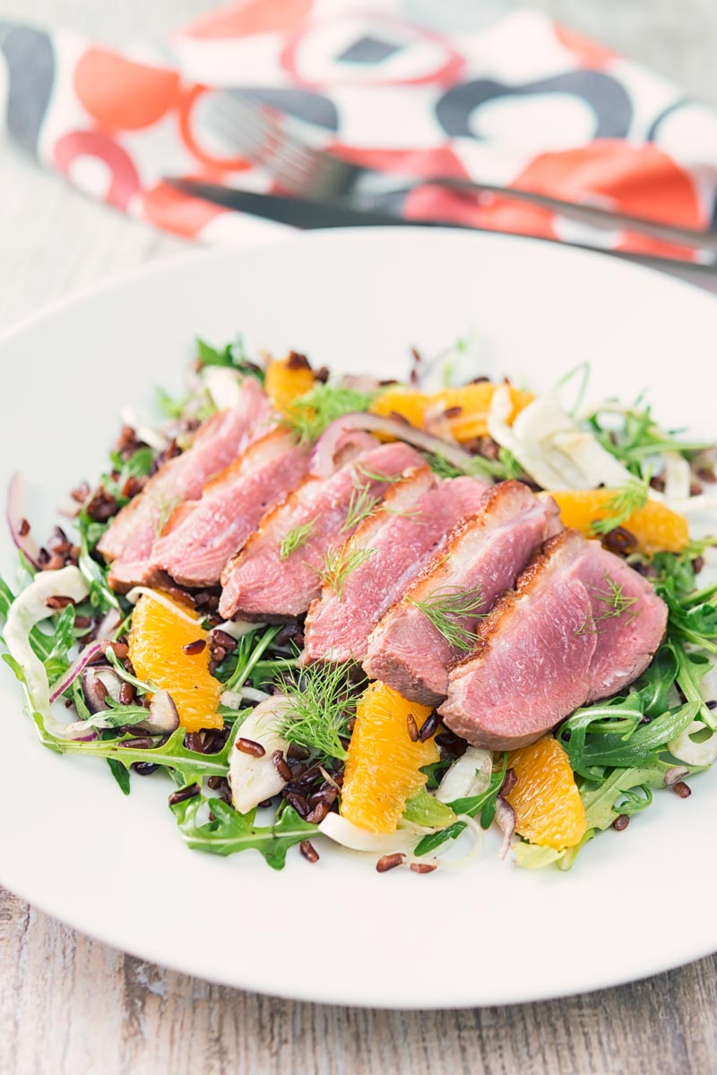 Portrait image of a fennel and orange salad served with a sliced rosy pink duck breast served on a white plate
