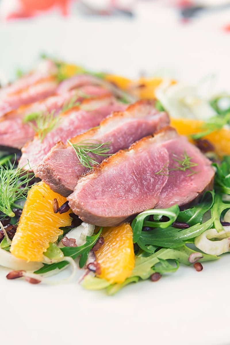 Portrait image of a fennel and orange salad served with a sliced rosy pink duck breast served on a white plate
