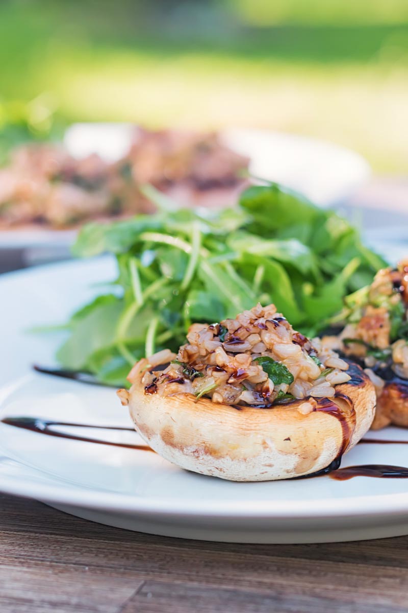 Portrait wide angle image of grilled stuffed mushrooms on a white plate with a rocket side salad with a garden scene in the background