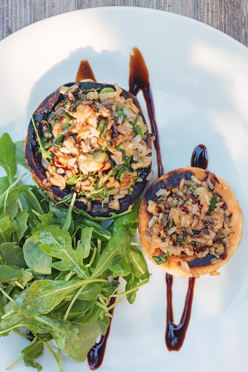 Portrait overhead image of grilled stuffed mushrooms on a white plate with a rocket side salad