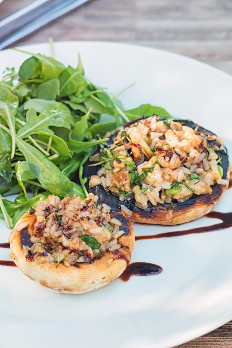 Portrait image of two grilled stuffed mushrooms on a white plate with a rocket side salad