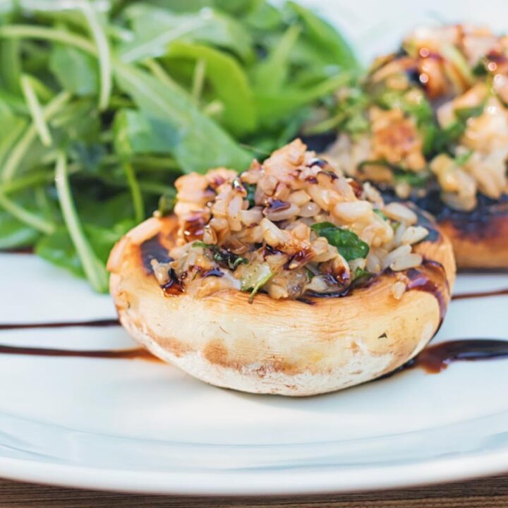Close up square image of grilled stuffed mushrooms on a white plate with a rocket side salad
