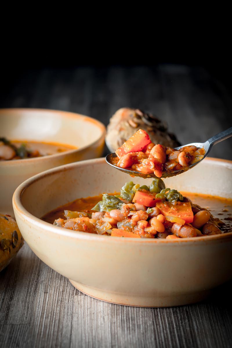 Portrait image of a diner taking a spoon of tomato and bean soup against a dark backdrop