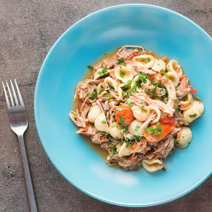 Square overhead image of a light shredded rabbit ragu with orecchiette pasta served in a blue bowl