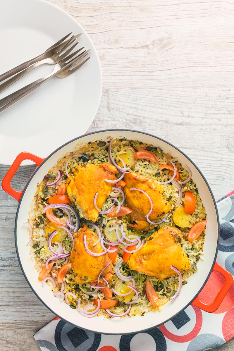 Tall overhead image of one pot chicken and rice featuring turmeric chicken thighs and red onion slivers