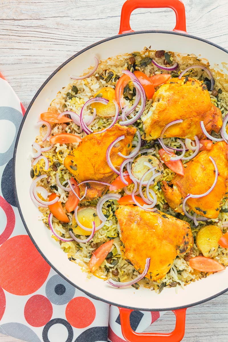 Tall close up overhead image of one pot chicken and rice featuring turmeric chicken thighs and red onion slivers