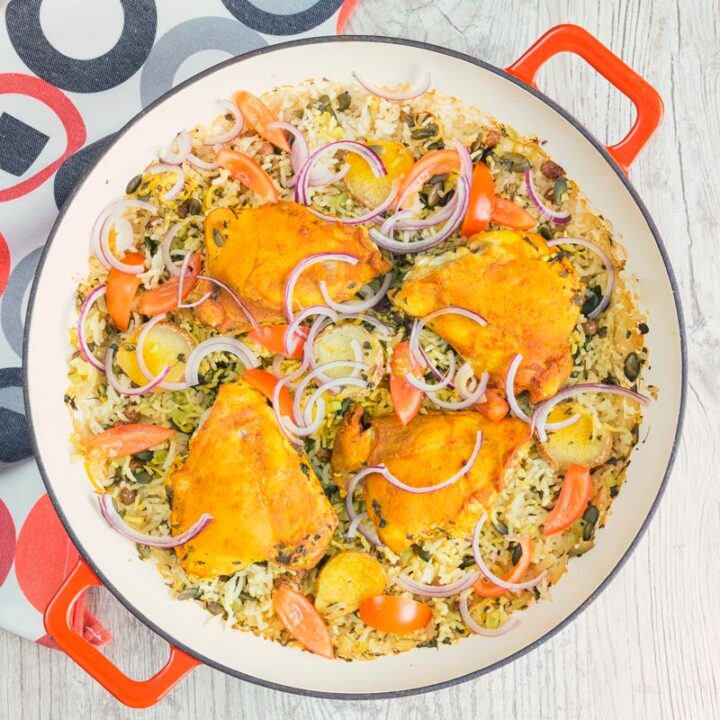 Square close up overhead image of one pot chicken and rice featuring turmeric chicken thighs and red onion slivers