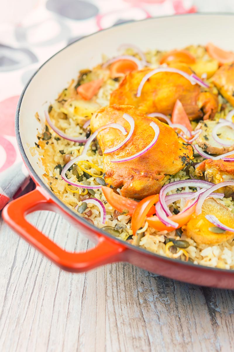 Tall close up image of one pot chicken and rice featuring turmeric chicken thighs and red onion slivers