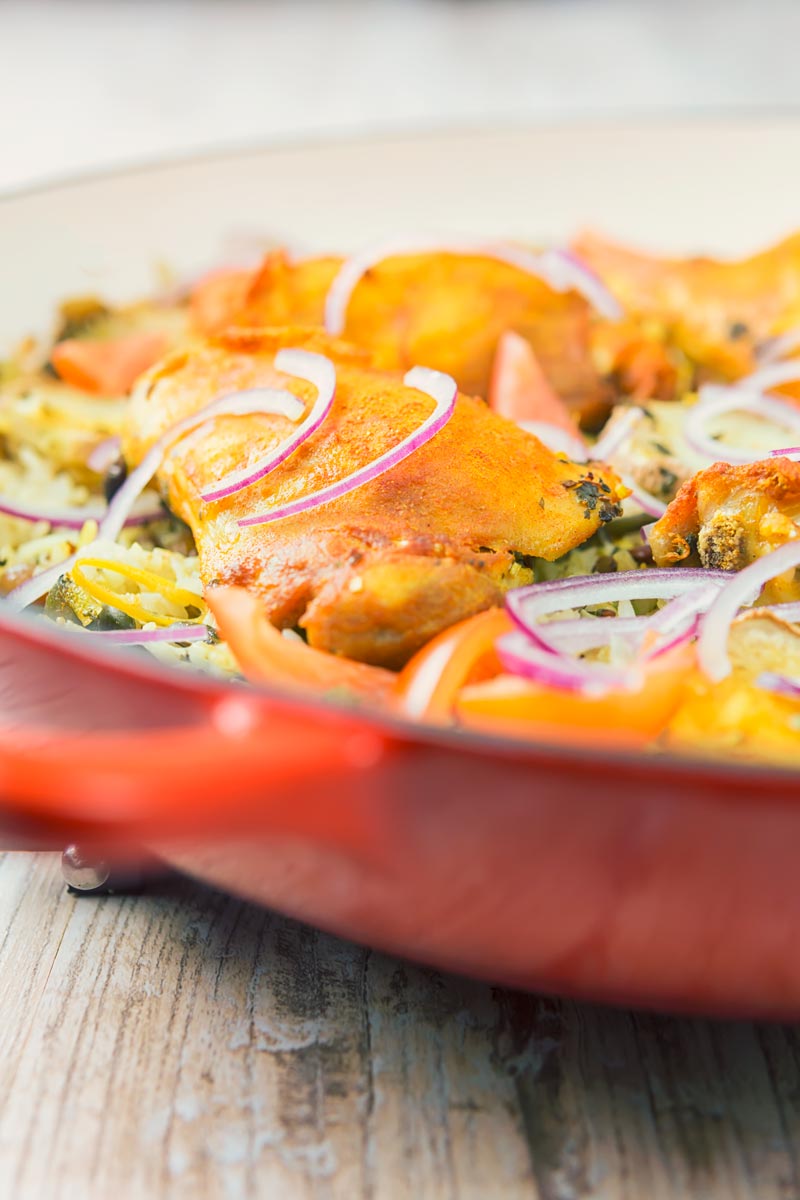 Abstract tall close up image of one pot chicken and rice featuring turmeric chicken thighs and red onion slivers