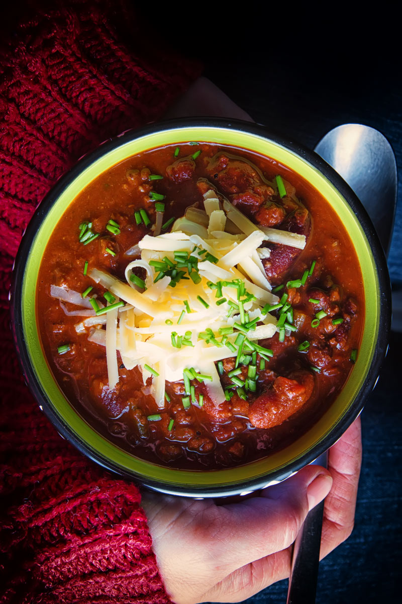 Chili Con carne topped with sour cream, cheese and chives in a bowl sat in a lap taken from above