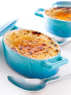 Tall close up image of an individual instant pot rice pudding cooked in blue serving pots with a brulee topping