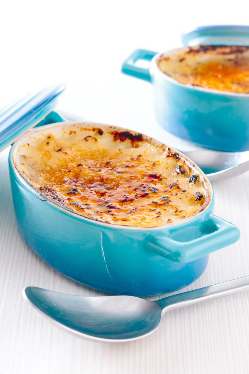 Tall close up image of an individual instant pot rice pudding cooked in blue serving pots with a brulee topping