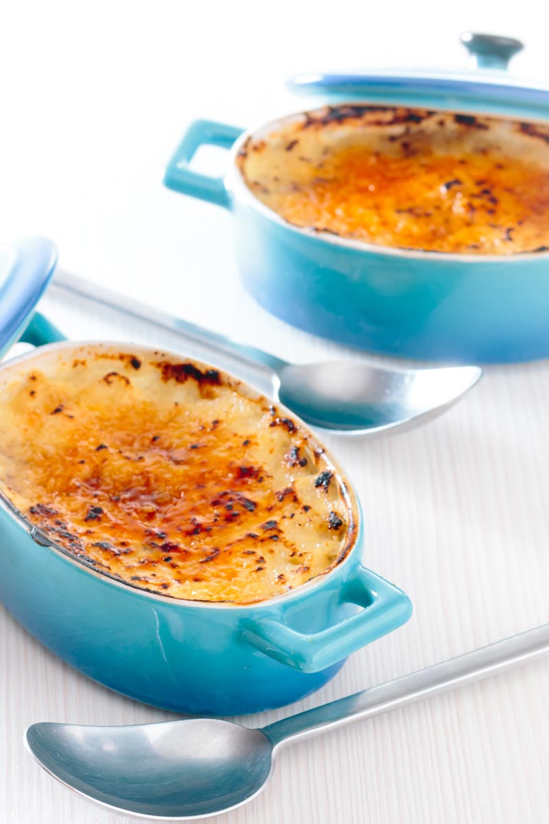 Tall image of two individual instant pot rice pudding cooked in blue serving pots with a brulee topping