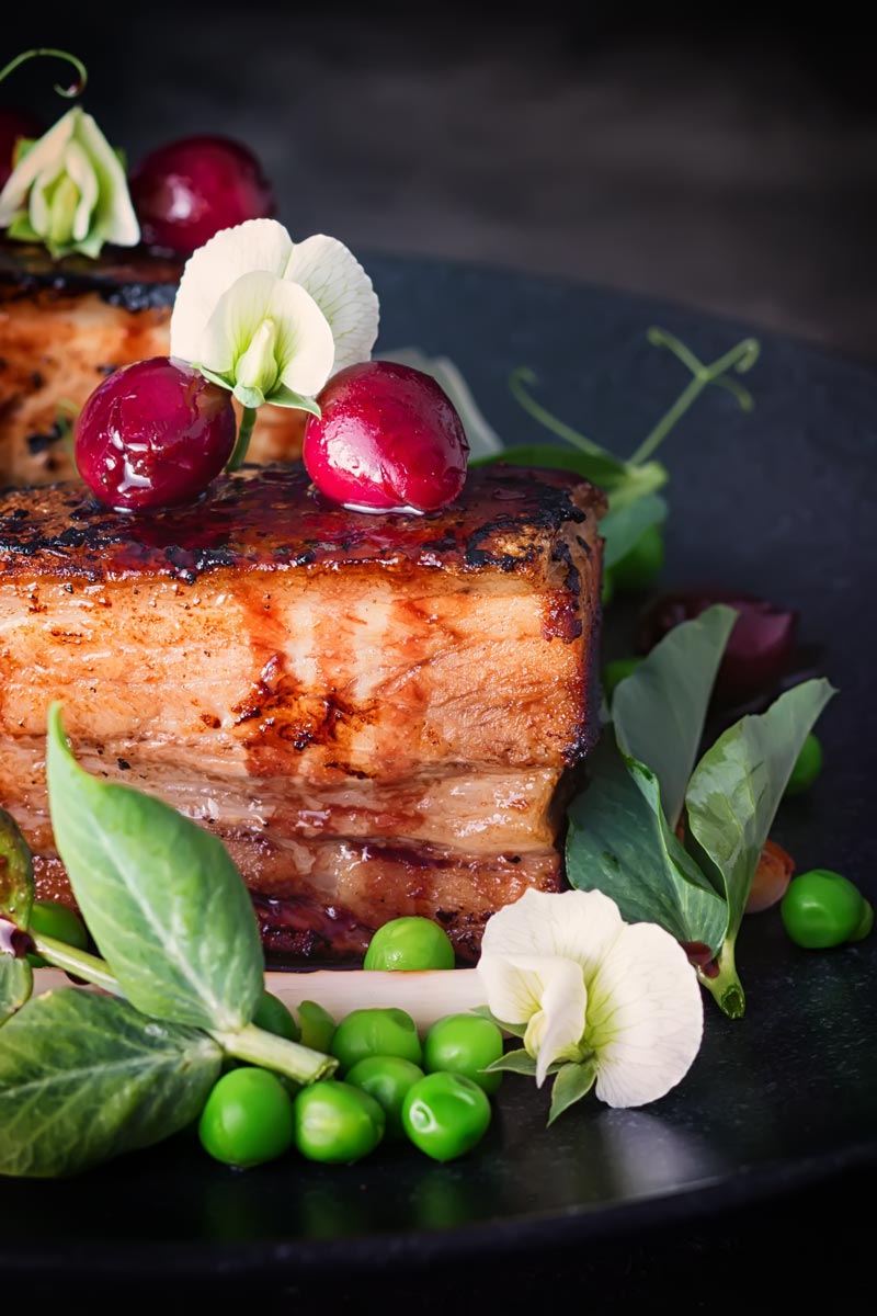Pressed pork belly with cherries, peas and pea shoots swerved on a black plate